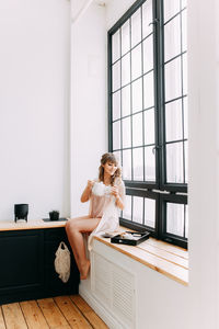A beautiful girl in pajamas prepares breakfast and pours coffee near the window of the house
