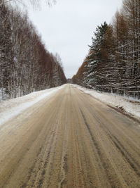 Dirt road amidst snow covered land against sky