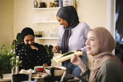 Happy young women in hijabs enjoying while preparing food in kitchen at home