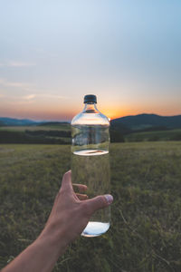 Cropped hand holding bottle against sky