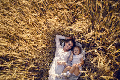  daughter with the mother lying on the ground on the field with ears in the evening in summer