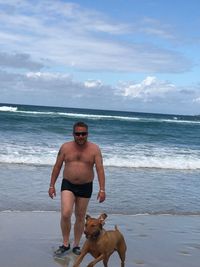 Portrait of shirtless man standing at beach against sky