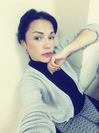 Portrait of young woman sitting against wall at home