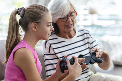 Grandmother and granddaughter talking to each other holding joysticks at home