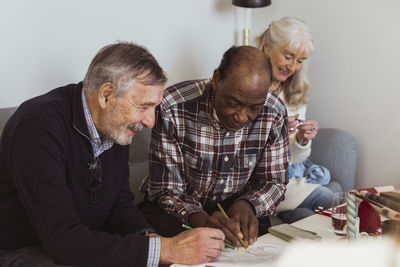 Smiling elderly men drawing on paper by female friend at nursing home