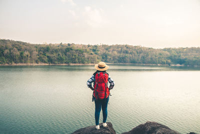 Rear view of man standing by lake against sky