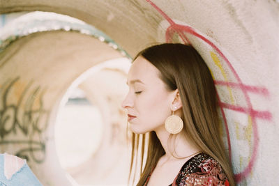 Side view of young woman with eyes closed sitting in concrete pipe