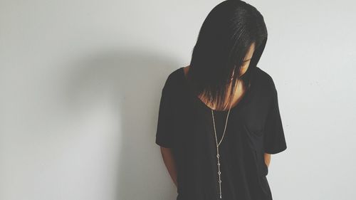 Woman looking down while standing against white wall