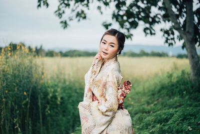Portrait of young woman wearing kimono standing on field