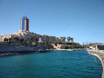 View of buildings by sea against clear blue sky