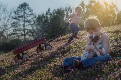 Cute girl with dog sitting on grass against trees