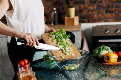 A woman cuts celery on a wooden board and transfers it to a transparent salad plate