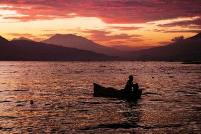 Silhouette men on boat in lake against sky during sunset