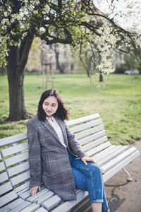 Cheerful asian young female student sitting on a bench under the blooming trees in spring park