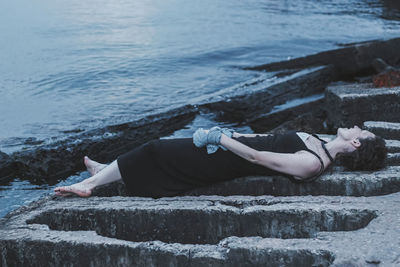 Full length of woman lying at retaining wall by sea