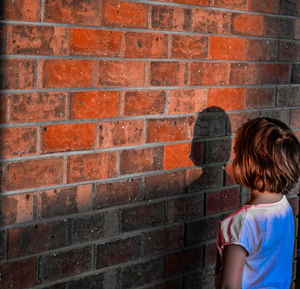 Rear view of girl looking against brick wall