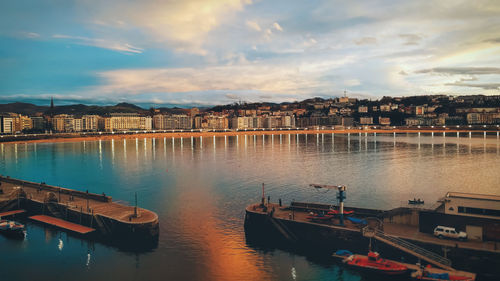 Boats in river by buildings against sky during sunset