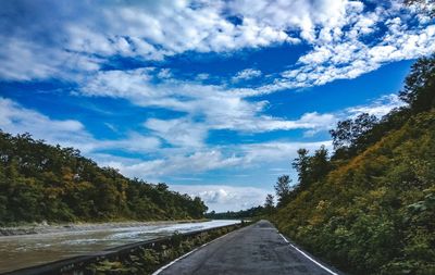 Empty road along plants and trees against sky