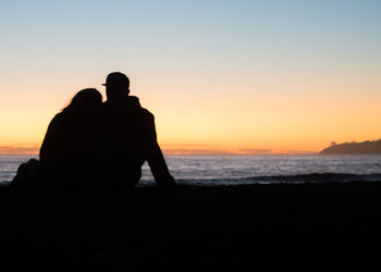 Rear view of silhouette couple on beach against sky during sunset