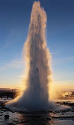 Geyser erupting against sky at sunset