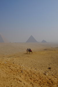 People riding motorcycle in desert against clear sky