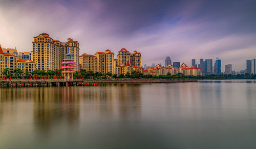 Illuminated buildings by river against sky in city