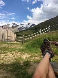 Low section of man relaxing on field against mountains