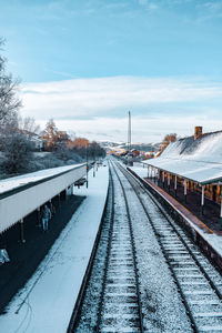 Snow covered railroad tracks at station against sky
