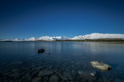 Scenic view of lake and mountains against clear blue sky