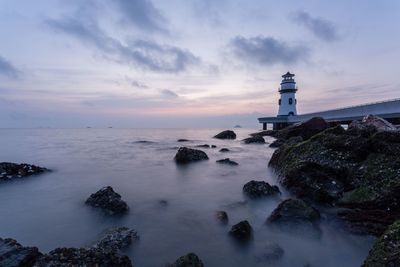 Lighthouse by sea against sky during sunset