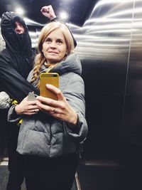 Young woman with friend taking selfie while standing at elevator