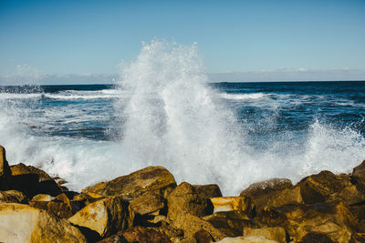 Waves splashing on rocks against clear sky