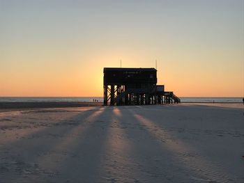 Built structure on beach against clear sky during sunset