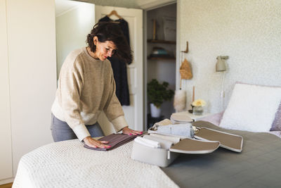 Smiling woman folding clothes on bed at home