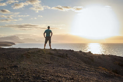 Man in  t-shirt looks at the sea and the sunset on the west coast of fuerteventura, near la pared