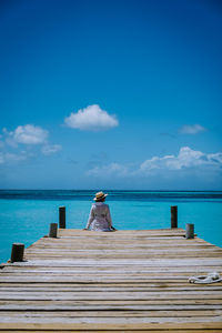 Rear view of woman sitting on pier over sea against blue sky