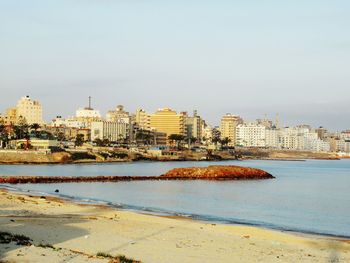 Buildings by sea against clear sky