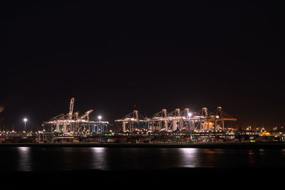 Illuminated port by sea against sky at night