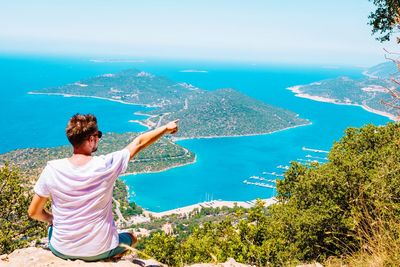 Rear view of man sitting on cliff against sea