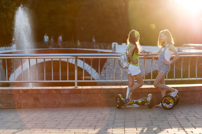 Friends with hoverboards standing by railing against bridge