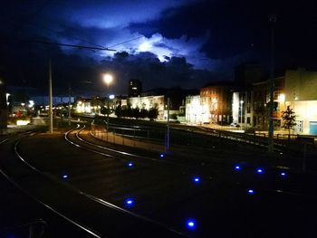 Illuminated railroad tracks in city against sky at night