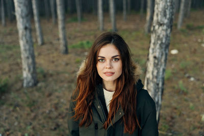 Portrait of beautiful young woman standing by tree trunk in forest