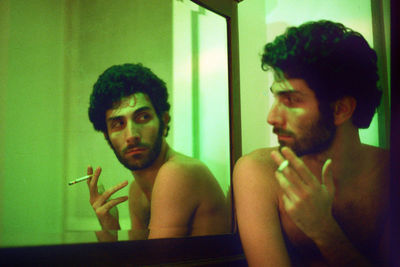 Shirtless man smoking cigarette while looking in mirror