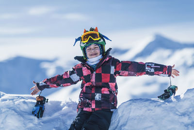 Happy boy with arms outstretched sitting against snowcapped mountain