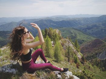 Young woman sitting on mountain against sky