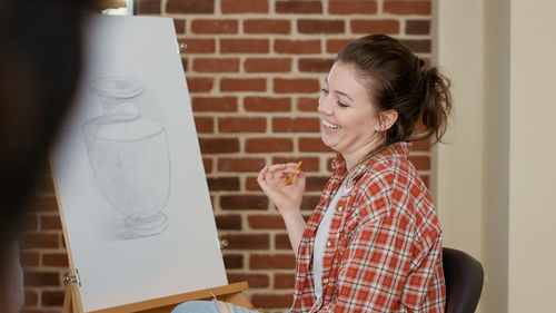 Side view of woman using digital tablet while standing against wall