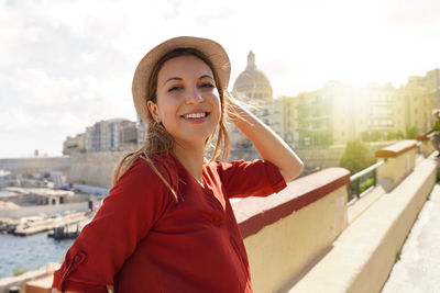 Portrait of smiling relaxed traveler woman walking along valletta seafront, malta