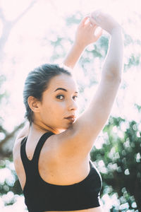 Portrait of young woman with arms raised during sunny day