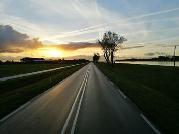 Road amidst field against sky during sunset