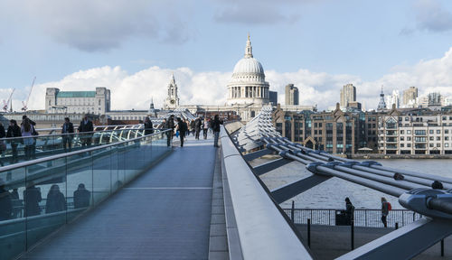 People on footbridge in city against sky